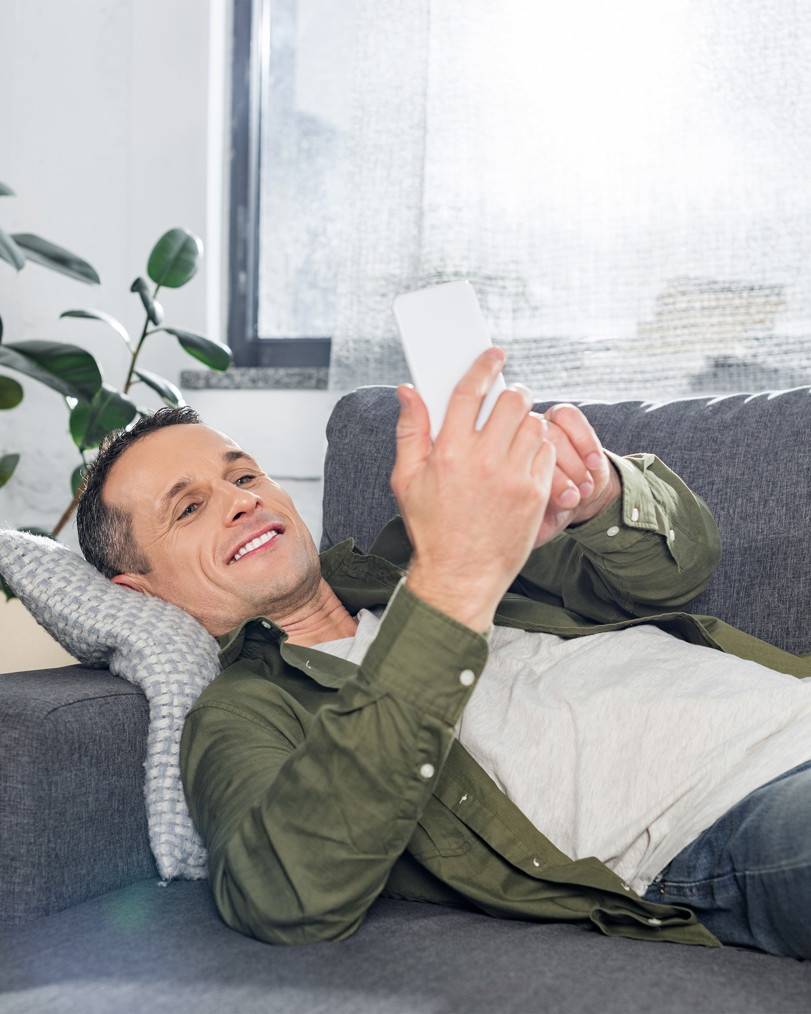 mies rentoutuu sohvalla selaten puhelinta
